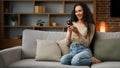 Smiling Hispanic Caucasian 30s woman housewife girl sitting on couch cozy sofa at home using smartphone for ordering Royalty Free Stock Photo