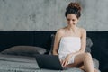 Smiling hispanic female shopping in online store at laptop sitting on bed after morning shower Royalty Free Stock Photo