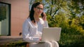 Smiling hispanic woman freelancer businesswoman girl student work on laptop talking mobile phone outdoors in city park Royalty Free Stock Photo