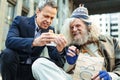 Smiling homeless elderly man eating burger from stranger