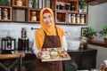 Smiling hooded Asian woman carrying a packing box of donuts