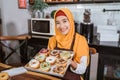 A smiling hooded woman carries a box packing of homemade donuts