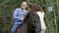 Smiling horseman sitting astride horse on green trees background on farm ranch. Happy stableman sitting on horseback