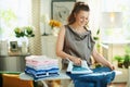 Smiling housewife with ironed clothes ironing on ironing board