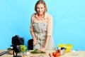 Smiling housewife stands in front of wooden table full of fresh vegetables