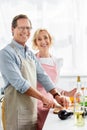 smiling husband cutting vegetables on wooden board in kitchen and looking