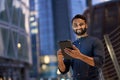 Smiling indian business man standing holding digital tablet in night city. Royalty Free Stock Photo