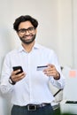 Smiling indian business man using phone holding credit card making e payment. Royalty Free Stock Photo