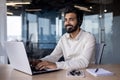 Smiling indian businessman in office setting with laptop and headset, professional at work Royalty Free Stock Photo