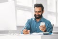 Smiling indian businessman using smartphone while writing notes Royalty Free Stock Photo