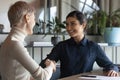 Smiling Indian businesswoman shaking client hand at meeting in office