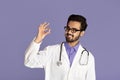Smiling Indian doctor in lab coat holding pill on violet background
