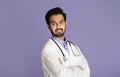 Smiling Indian doctor in lab coat standing with crossed arms on violet background