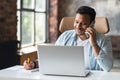 Smiling indian freelancer guy is talking on smartphone and taking notes Royalty Free Stock Photo