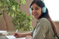 Smiling indian girl wear headphones look at camera study at home listen course.
