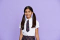 Smiling indian kid girl wear school uniform stand on lilac background, portrait. Royalty Free Stock Photo