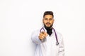 Smiling indian male doctor in white coat with stethoscope pointing finger to you over grey background Royalty Free Stock Photo