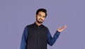 Cheerful Indian man presenting something on violet background, space for your product design