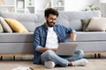 Smiling Indian man using laptop while sitting cross-legged on floor at home Royalty Free Stock Photo