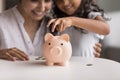 Smiling Indian mom and little daughter dropping coins into piggybank Royalty Free Stock Photo