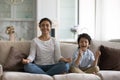 Smiling Indian mother with 5s son meditating on couch together