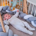 Smiling infant baby boy playing with a wooden mobile suspended above the crib. Happy child playing in bed with toys Royalty Free Stock Photo