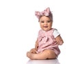 Smiling Infant baby toddler in polka dot dress and headband with bow sits on the floor holding hand up