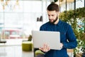 Smiling intelligent man with laptop in hand in office