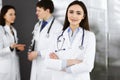 Smiling intelligent woman-doctor is standing with arms crossed in a clinic, together with her colleagues at the