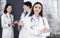 Smiling intelligent woman-doctor is standing with arms crossed in a clinic, together with her colleagues at the