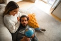 Smiling international millennial couple rest on sofa, looking at globe, choose country for vacation