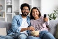 Smiling interracial spouses sitting on couch at home, watching tv Royalty Free Stock Photo