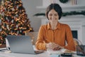 Smiling italian female making notes, using laptop at home office during christmas holidays
