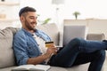 Smiling jewish guy using laptop and credit card at home