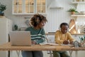 Smiling black mother helping small pensive son with school tasks studying together at kitchen table