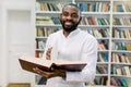 Smiling joyful male african american university student standing in modern reading hall of college library, holding open Royalty Free Stock Photo