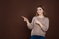 Smiling joyful woman in loose sweater posing against brown studio wall pointing at copy space for advertisment or