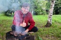 smiling, joyful young man roasts meat, cook barbecue, delicious crispy meat barbecue metal grill coals nature against background