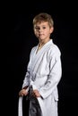 Smiling karate kid in brand new kimono, posing on the black background. Karate fighter holding his belt Royalty Free Stock Photo