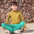 Smiling kid boy sitting on skateboard outdoors Royalty Free Stock Photo