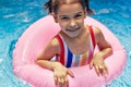 Smiling kid in a colorful swimsuit relaxing on an inflatable pink ring floating in a pool during summer vacation. Joyful little Royalty Free Stock Photo