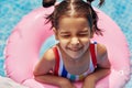 Smiling kid in a colorful swimsuit relaxing on an inflatable pink ring floating in a pool during summer vacation. Joyful little Royalty Free Stock Photo