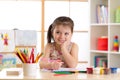 Smiling kid girl drawing with color pencils in day care center