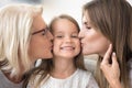 Smiling kid girl enjoys mom and grandma kissing on cheeks