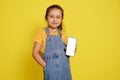 Smiling kid girl holds a smart mobile phone with white blank mockup digital touch screen. Copy ad space for mobile app Royalty Free Stock Photo