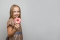 Smiling kid girl standing with pink glazed donut, studio portrait. Holiday birthday party concept