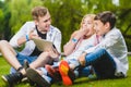 Smiling kids having fun and look to tablet at grass. Children playing outdoors in summer. teenagers communicate outdoor Royalty Free Stock Photo