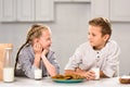 smiling kids looking at each other and sitting at table with cookies and milk