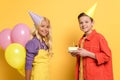 Kids with party caps holding balloons and plate with birthday cake on yellow background Royalty Free Stock Photo