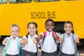 Smiling kids showing thumbs up in front of school bus